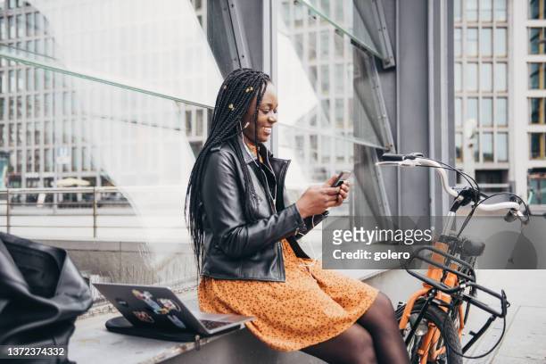 black business woman with mobile sitting outdoors in berlin - bicycle rental stockfoto's en -beelden