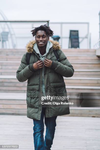 happy smiling  fashionable man in warm clothes and backpack walking on street near wooden bench. - messestand bildbanksfoton och bilder