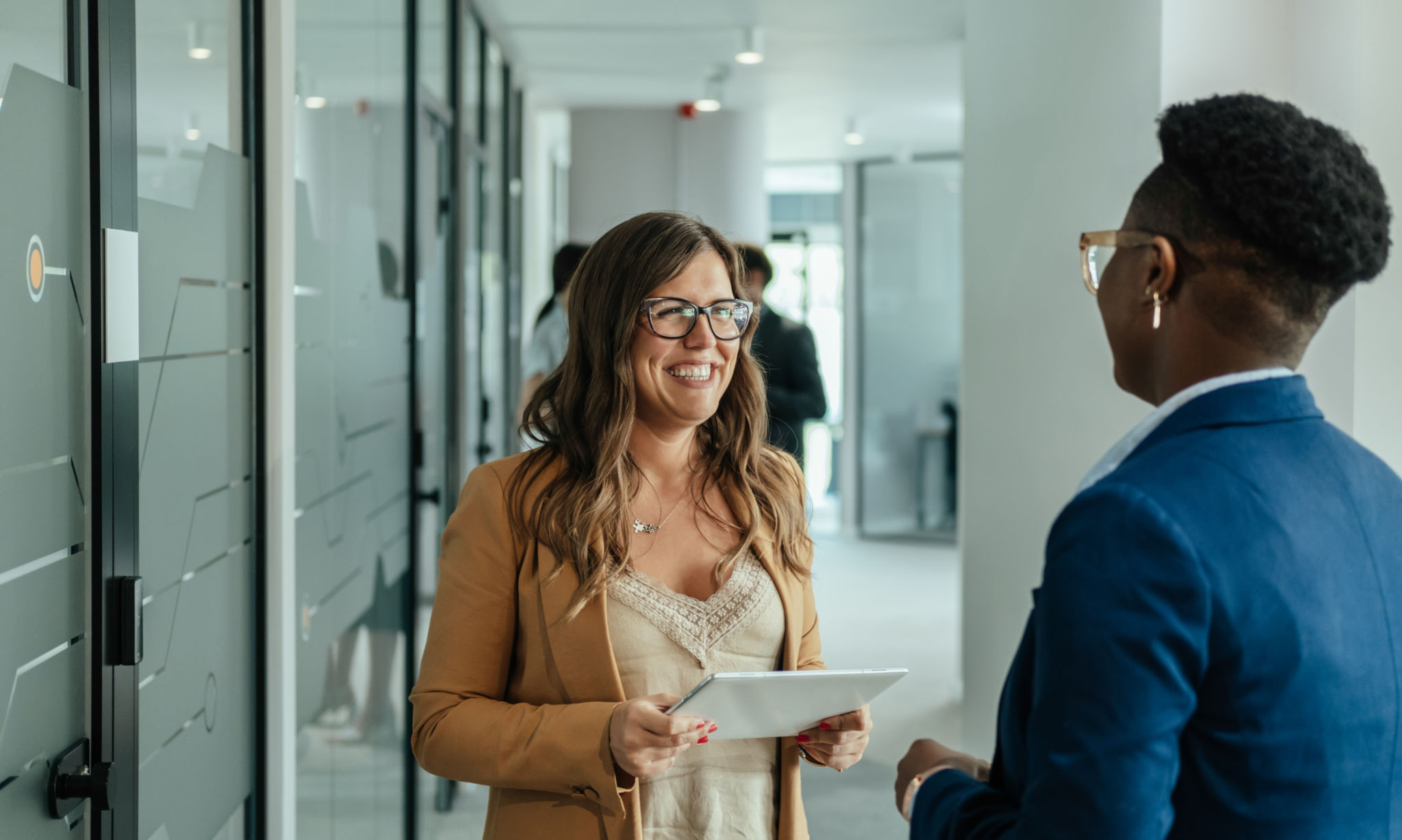 Happy Businesswoman Holding Digital Tablet and Talking with her Anonymous Female Colleague at Work Happy Businesswoman Holding Digital Tablet and Talking with her Anonymous Female Colleague at Work