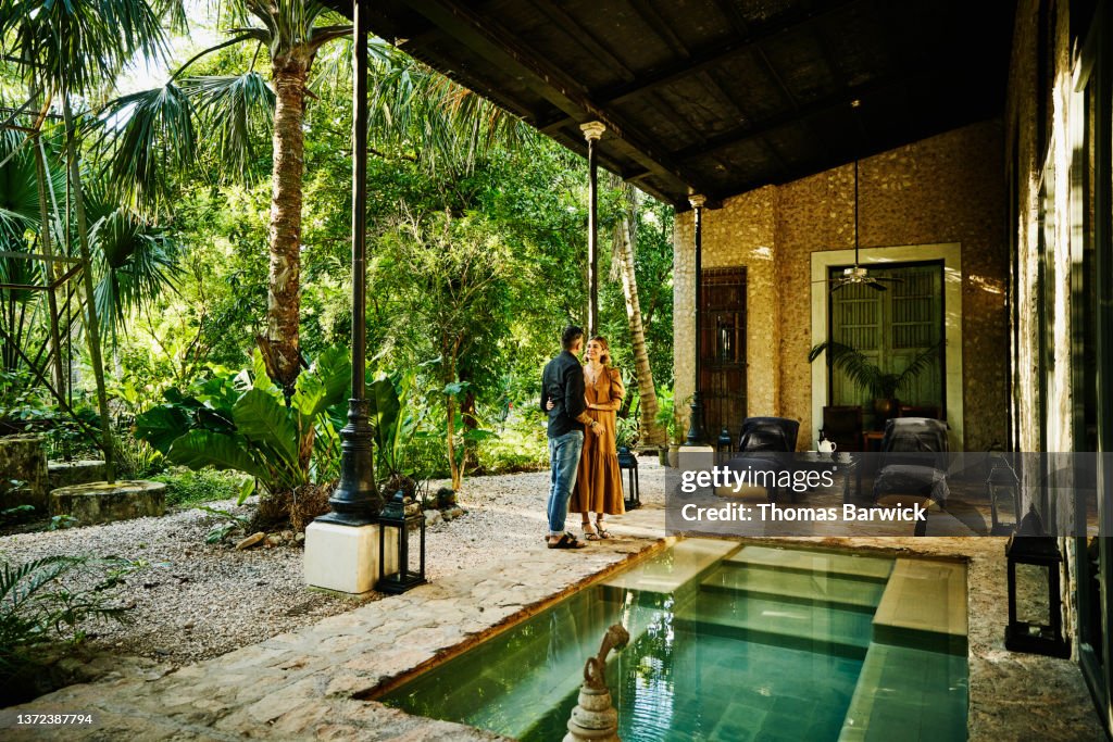 Wide shot of smiling couple embracing by plunge pool at luxury tropical hotel