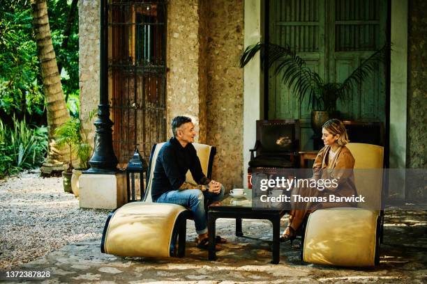 wide shot of smiling couple enjoying tea in garden of luxury tropical hotel - woman elegant crossed legs stock pictures, royalty-free photos & images