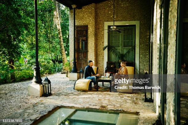 Wide shot of smiling couple relaxing by plunge pool at luxury tropical hotel