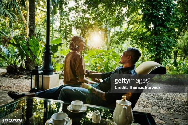 medium wide shot of couple relaxing in lounge chair at luxury tropical hotel at sunset - premium tea bildbanksfoton och bilder