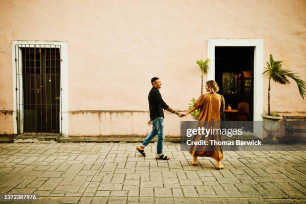 wide shot of smiling couple holding hands and walking down street while exploring town during vacation - 40 44 anni foto e immagini stock