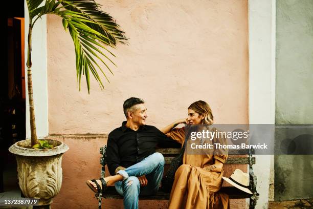 medium wide shot of smiling couple relaxing on bench while exploring town during vacation - couple short hair stock-fotos und bilder