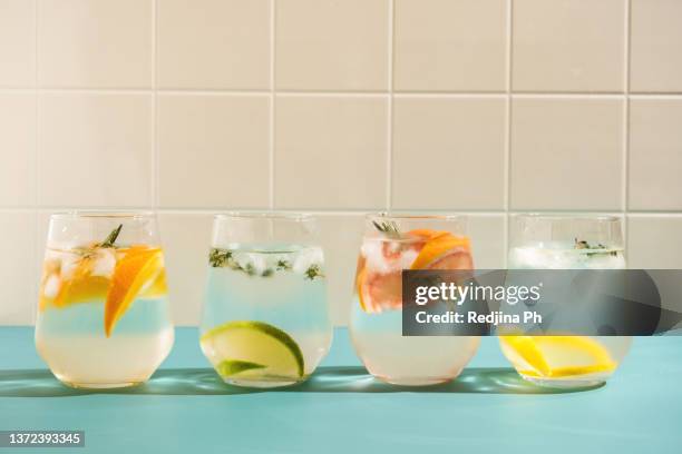 summer refreshing sparkling drink with ice, fresh fruits and herbs: rosemary, thyme, orange, lime, lemon, grapefruit in transparent glasses on a blue background. - soda fotografías e imágenes de stock