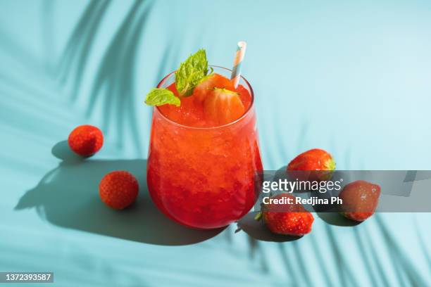 summer refreshing sparkling drink with melted ice, fresh strawberry and drinking straw and mint in transparent glasses on blue background. - mint green stock pictures, royalty-free photos & images