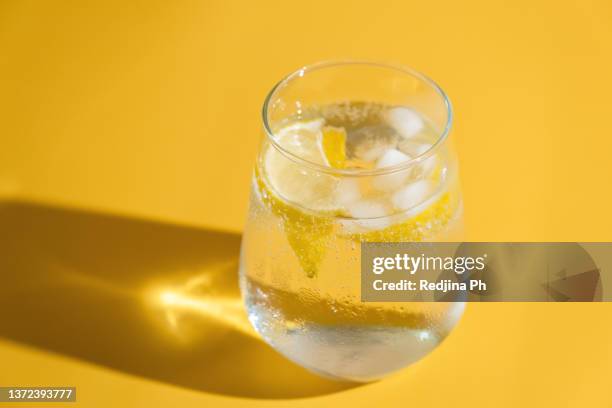 summer refreshing sparkling drink with ice cube, fresh fruit lemon in transparent glasses on green background. cold summer citrus ice water. - sparkling water glass stock-fotos und bilder