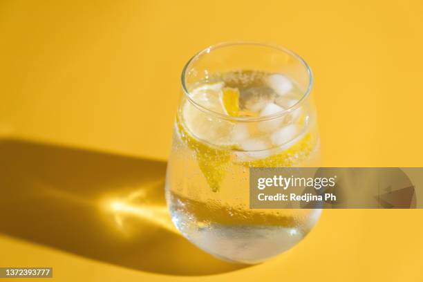 summer refreshing sparkling drink with ice cube, fresh fruit lemon in transparent glasses on green background. cold summer citrus ice water. - koolzuurhoudend water stockfoto's en -beelden