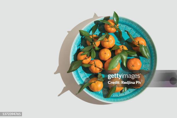 orange tangerines with leaves in a blue plate on a white solid background. the concept of winter comfortable festive food. top view. flat lay. - blue plate stock pictures, royalty-free photos & images