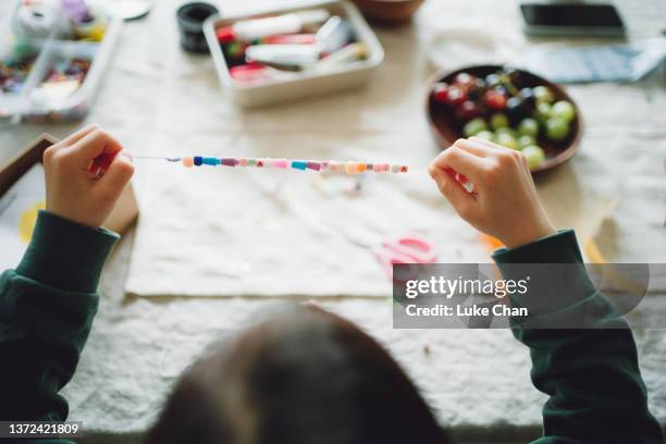 自宅でブレスレットを作るためにビーズを選ぶアジアの小さな女の子 - bracelet ストックフォトと画像