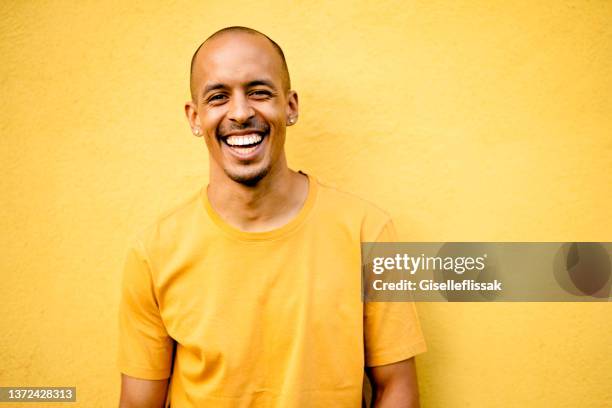 junger mann lacht, während er ein gelbes hemd an einer gelben wand trägt - farbige wand stock-fotos und bilder