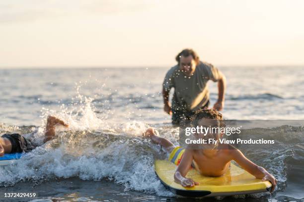 feliz body boarding de niño en la playa con su padre - bodyboard fotografías e imágenes de stock