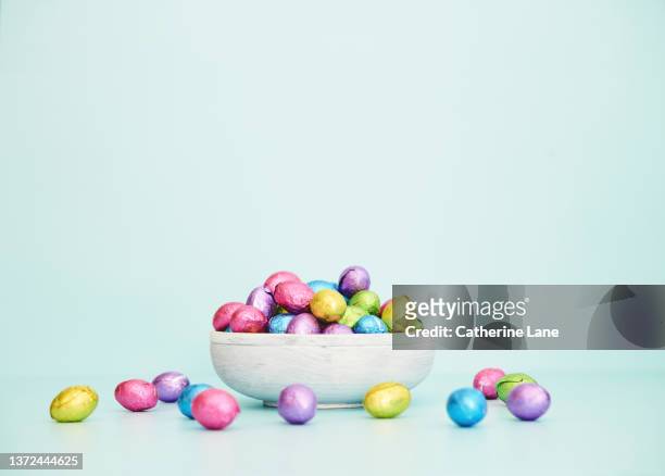 easter background with whitewashed wooden bowl filled with foil covered chocolate easter eggs - huevo de pascua de chocolate fotografías e imágenes de stock