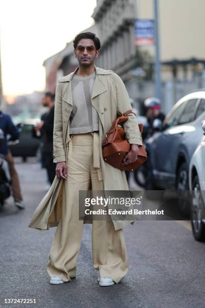 Rahi Chadda wears brown sunglasses, a beige wool pullover, a beige long coat, a camel shiny leather large handbag, pale yellow high waist belted /...