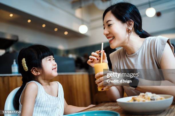 young asian mother and lovely little daughter having lunch together in a cafe, sharing mango smoothie and pasta. they are talking and looking at each other smiling joyfully. mother and daughter relationship. family and eating out lifestyle - mother daughter brunch bildbanksfoton och bilder