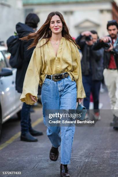 Gala Gonzalez wears a gold chain pendant necklace, a brown V-neck bra underwear, a gold shiny silk oversized blouse / shirt, a black shiny leather...