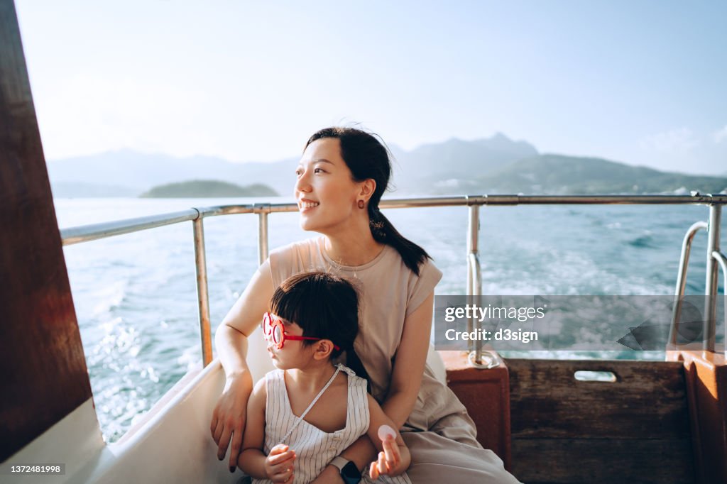 Young Asian mother and lovely little daughter with red sunglasses enjoying a yacht ride over nice calm sea on a summer day. Looking over and relaxed at the sea. Family lifestyle. Enjoying outdoor fun, boat trip and sea vacations