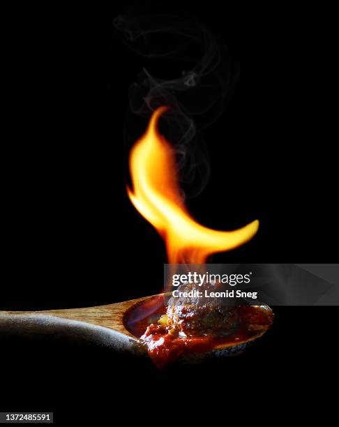 meatball with spicy tomato sauce in wooden spoon with fire shaped as pepper side view on black background isolated closeup. selective focus - cultivated meat stock pictures, royalty-free photos & images