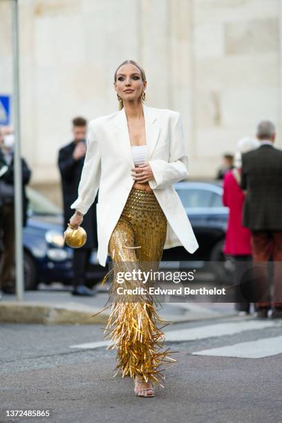 Leonie Hanne wears gold large pendant earrings, a white embossed ribbed shoulder-off / cropped top, a white latte long oversized blazer jacket, a...