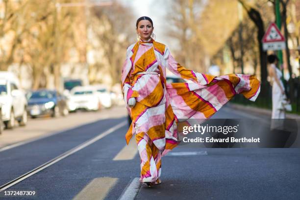 Alexandra Pereira wears gold and yellow large circle earrings from Fendi, gold earrings, a pale pink / orange / white / fuchsia print pattern flowing...