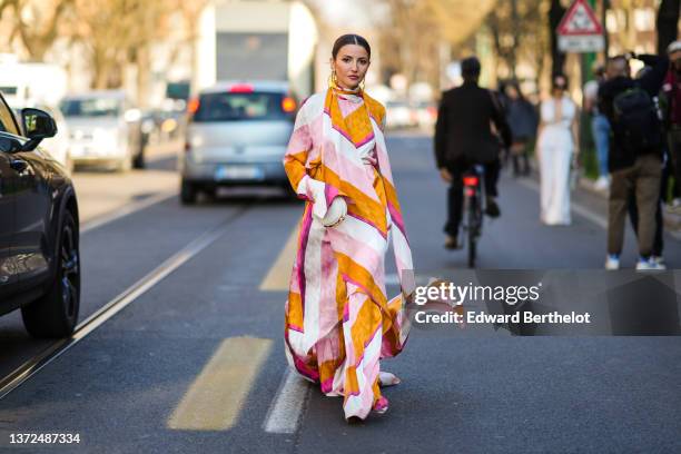 Alexandra Pereira wears gold and yellow large circle earrings from Fendi, gold earrings, a pale pink / orange / white / fuchsia print pattern flowing...