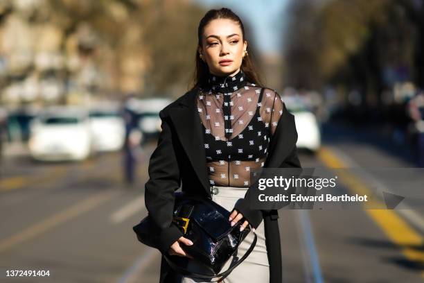 Merve Gorgoz wears gold large earrings, a black tulle with white embroidered logo pattern turtleneck t-shirt from Fendi, a black long oversized...