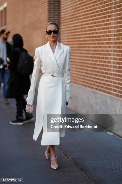 Caroline Daur wears black sunglasses from Fendi, silver and rhinestones pendant earrings, a white long blazer coat from Fendi, a white shiny leather...