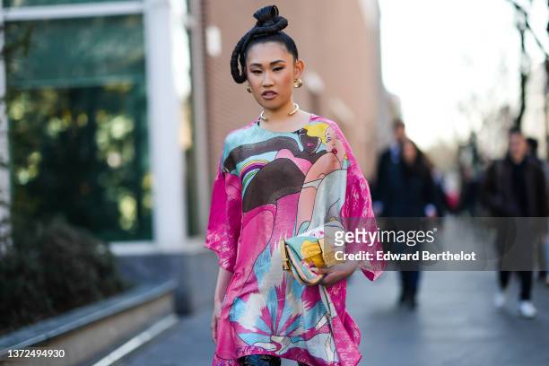 Jaime Xie wears gold earrings, a gold large necklace, a pink / pale blue / yellow / black / beige woman print pattern with a rainbow flowing bat...