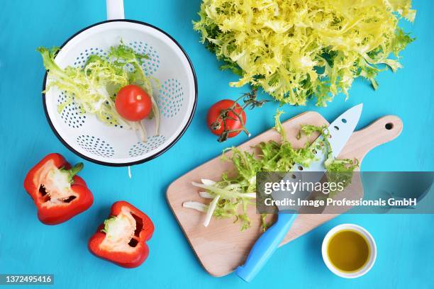 various salad ingredients: frisee lettuce, tomatoes, peppers and olive oil - krulandijvie stockfoto's en -beelden