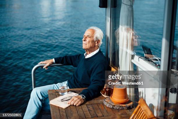 senior man sitting by table at houseboat on sunny day - newspaper on table ストックフォトと画像