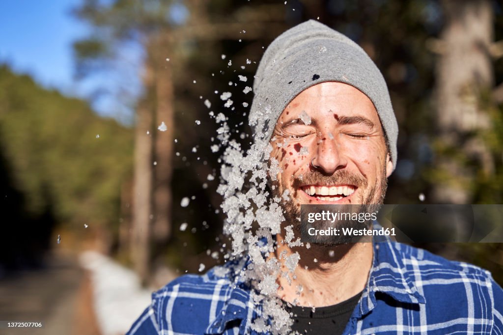 Cheerful man with eyes closed enjoying amidst falling snow