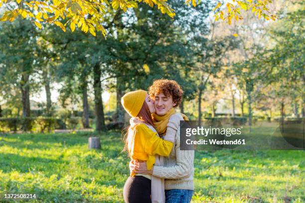 woman kissing boyfriend on cheek at autumn park - capelli rossi foto e immagini stock