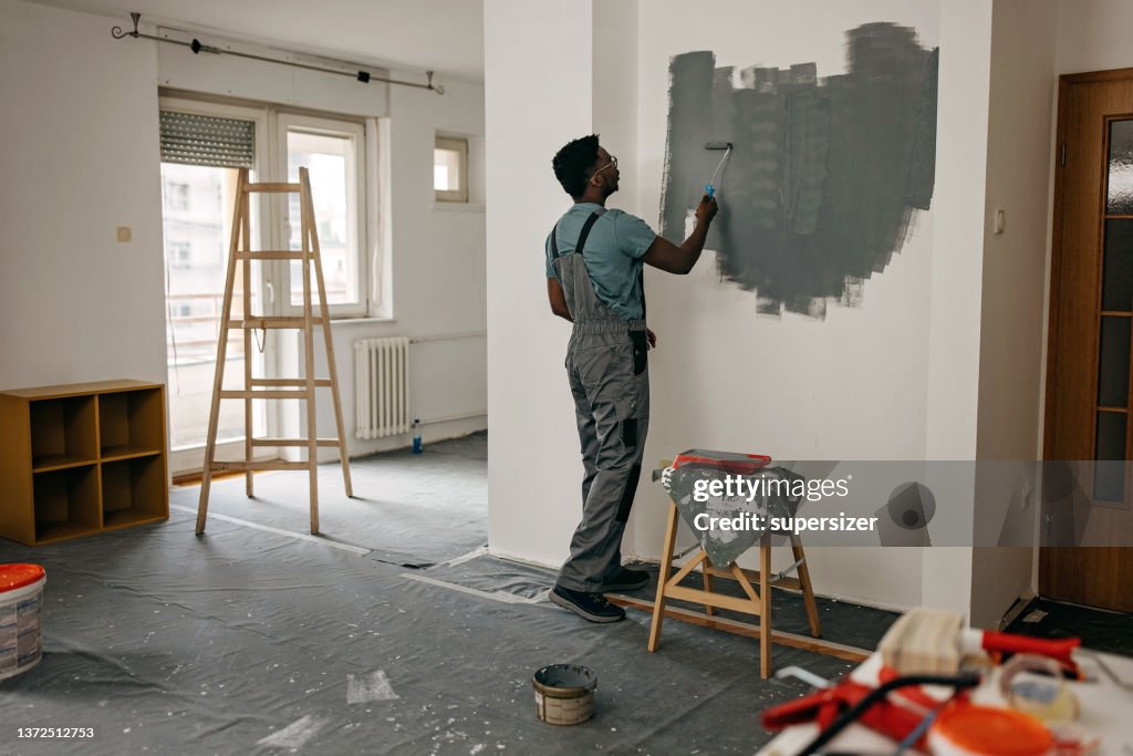 African-American professional painter paints the wall indoors