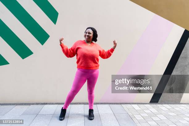 smiling woman flexing muscles in front of wall - autoriteit stockfoto's en -beelden