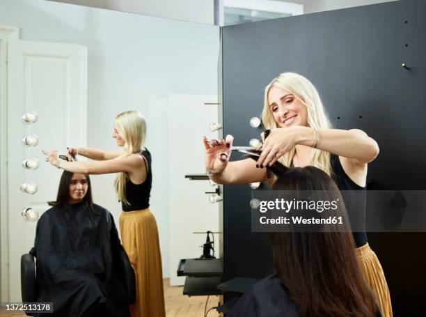 smiling hairdresser cutting customer's hair in salon - friseurberuf stock-fotos und bilder