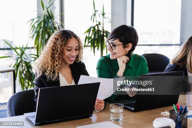 happy businesswomen reviewing financial report with laptops at desk in coworking office - finanzbericht stock-fotos und bilder