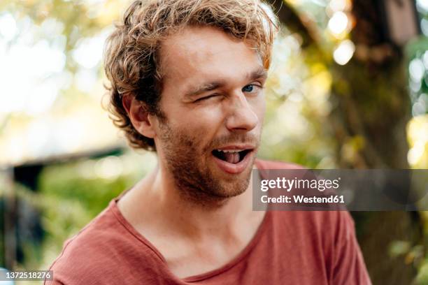 young man winking eye outdoors - winking fotografías e imágenes de stock