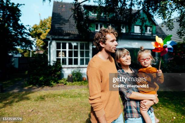 parents looking at daughter with multi colored pinwheel in garden - gartenhaus stock-fotos und bilder