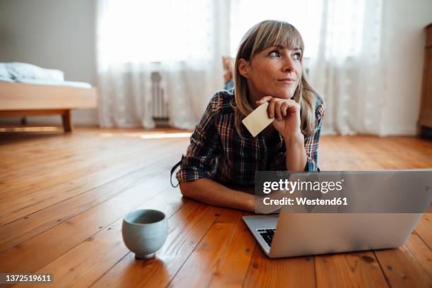 thoughtful woman with credit card and laptop lying on floor at home - thinking of you card stock-fotos und bilder