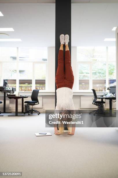 businesswoman doing handstand in front of a column at office - businesswoman handstand stock-fotos und bilder