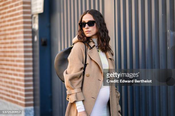 Erika Boldrin wears black sunglasses from Gucci, a pale pink / yellow / green print pattern tube dress with long sleeves, a beige oversized long coat...