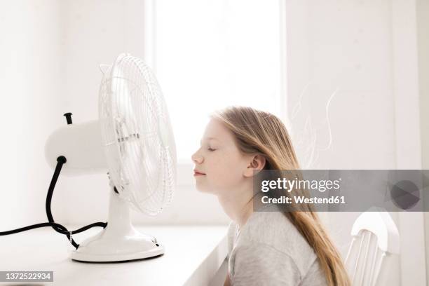 girl sitting in front of table with electric fan at home - table fan stock pictures, royalty-free photos & images