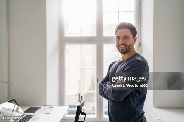 smiling confident businessman with arms crossed in office - un seul homme d'âge moyen photos et images de collection