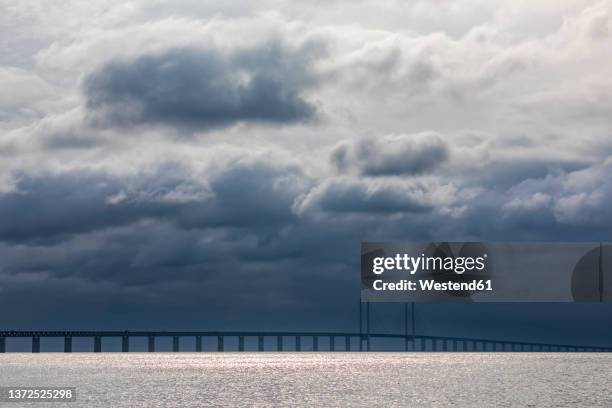 cloudy sky over sound strait with silhouette of oresund bridge in background - oresund bridge stock pictures, royalty-free photos & images
