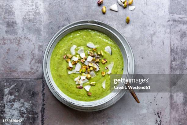 studio shot of bowl of vegan pea soup with zucchini, broccoli, pistachios and coconut shreds - calabacín fotografías e imágenes de stock