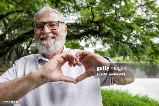 um homem idoso fazendo um símbolo de coração com as mãos - heart - fotografias e filmes do acervo