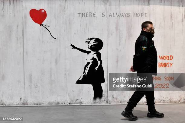 Man walks near a Banksy artwork during the "The World of Banksy" Art Exhibition at Porta Nuova Railway Station on February 24, 2022 in Turin, Italy.
