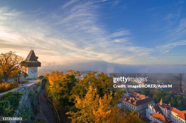cityscape of graz and the famous clock tower (grazer uhrturm) on shlossberg hill, graz, styria region, austria, in autumn, at sunrise - turmuhr stock-fotos und bilder