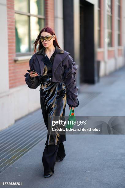 Guest wears yellow and black sunglasses, a black shiny varnished leather long coat, a dark cropped oversized jacket, black large flared pants, a...
